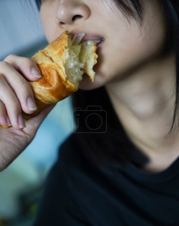 Photo for Woman eating a croissant in her hand, closed up shot. - Royalty Free Image