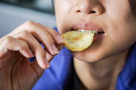 Photo for Woman using her hand to eat potato chips from a bowl, closed up shot. - Royalty Free Image