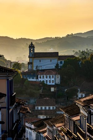 Photo for Old church seen in the city of Ouro Preto during sunset with its houses in colonial architecture, roofs and the mountains in the background - Royalty Free Image