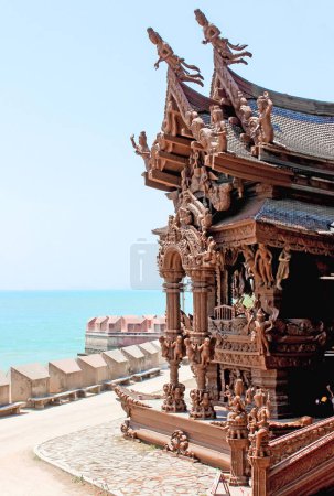 Ornate architectural handcrafted wooden temple by the seaside, bathed in bright sunlight under a clear sky.