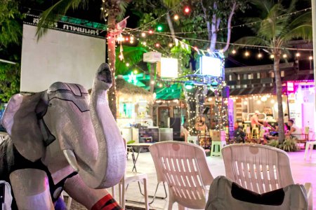 Ein lebendiges Café im Freien bei Nacht mit einer Elefantenstatue, beleuchteten Dekorationen und einer farbenfrohen Atmosphäre