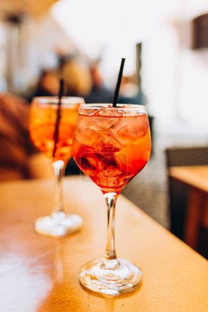 Photo for Mezcal Negroni and Aperol Spritz Cocktails. Alcoholic beverage based on table with ice cubes outdoors. Served cocktail with slice and straw placed on wooden table of sidewalk cafe in Italy - Royalty Free Image
