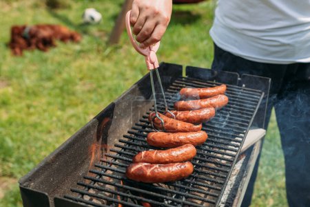 Grilled pork sausage on a cast iron grill. Hand of young woman grilling some meat. Young female having a barbecue, girl preparing food outdoors