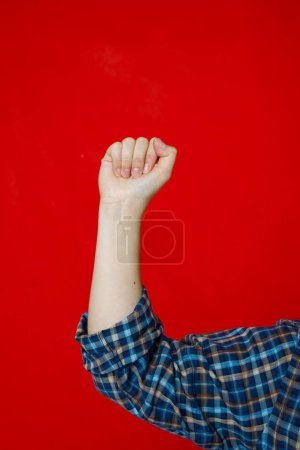 Frauenhand isoliert auf rotem Hintergrund. Frauenpower, erhobene geballte Faust