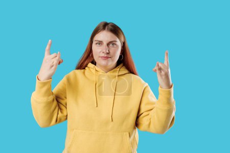 Young brunette 30s woman makes rock n roll sign isolated on blue background, studio portrait