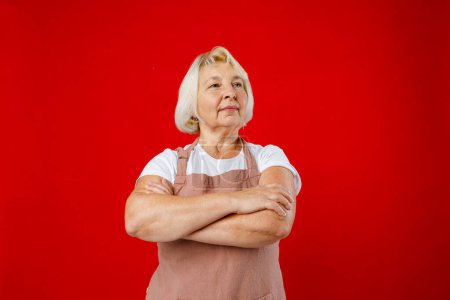 Housewife female chef cook confectioner in apron standing on red background in studio. Crossed arms.