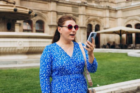 Retrato de mujer con cara confusa, caminando por la calle, sosteniendo el teléfono inteligente, sintiéndose perdida, usando la aplicación de mapa móvil