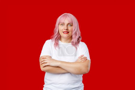 Excited happy woman with pink hair standing on red background in studio. Crossed arms.