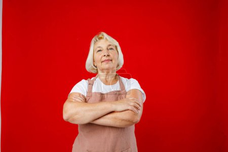 Housewife female chef cook confectioner in apron standing on red background in studio. Crossed arms.