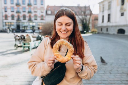 Atractiva joven turista de 30 años está sosteniendo bagel, tradicional bocadillo polaco en Cracovia. Viajando por Europa en primavera. Enfoque selectivo.