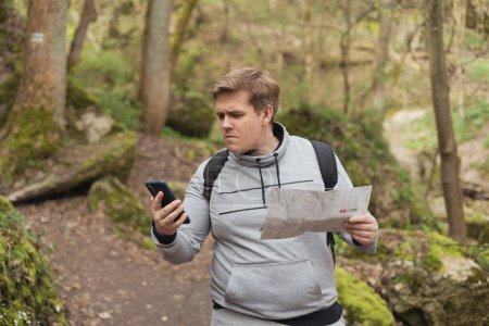 A young man tries to find a phone signal in the forest. Searching for mobile connection in wild nature on vacation. Angry man tourist hiker holding smart phone searching signal