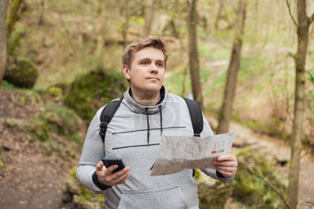 A young man tries to find a phone signal in the forest. Searching for mobile connection in wild nature on vacation. Angry man tourist hiker holding smart phone searching signal