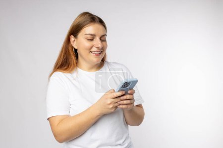 Lächelnde junge brünette Frau mit Smartphone, die isoliert auf weißem Hintergrund posiert, Studioporträt. Nette schöne Frau im Handy-Chat