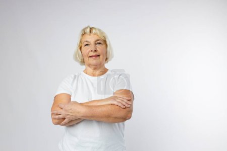 Beautiful senior blonde woman smiling and looking at camera over white background. Human emotions, facial expression concept