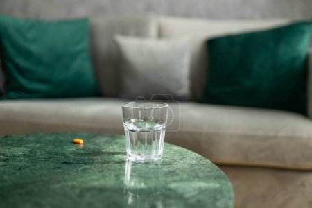 Tabletten und ein Glas Wasser auf dem Tisch. Modernes und komfortables Wohn- oder Hotelzimmer-Interieur mit Sofa. Gesunder Lebensstil.