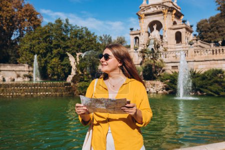 Joven turista femenina con mapa de papel y teléfono visitando el Parque de la Ciutadella en Barcelona. Concepto de viaje, turismo y vacaciones en la ciudad, Viajar por Europa