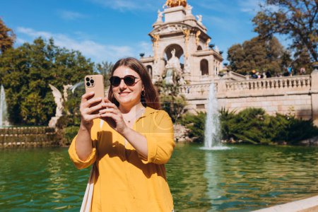 Young female tourist visiting Ciutadella Park in Barcelona. Young traveling woman taking selfie outdoors. Concept of travel, tourism and vacation in city