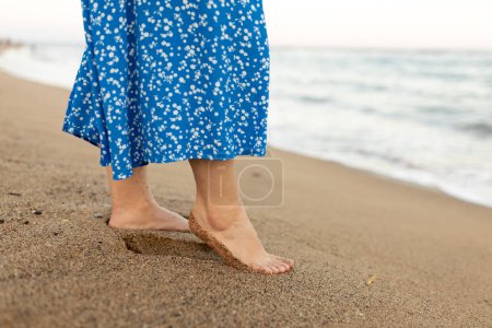 Frau geht am Sandstrand spazieren. Wellenbewegungen kommen an den Fuß, schäumende Meeresbeschaffenheit. Sommer- und Urlaubskonzept.