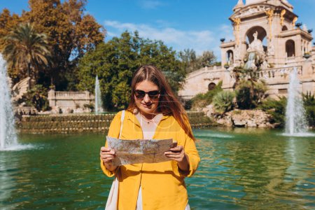 Jeune touriste féminine avec carte papier et téléphone visitant le parc Ciutadella à Barcelone. Concept de voyage, tourisme et vacances en ville