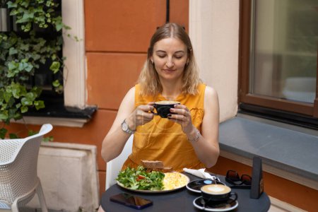 Porträt einer jungen blonden Frau, die am Tisch im Café Kaffee trinkt. Entspannen und nachdenken beim Kaffeetrinken. Konzept des leichten Frühstücks.