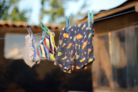 Das Foto zeigt Kinderkleidung, die nach dem Waschen draußen getrocknet wird. Die leuchtenden Farben der Kleidung vor dem Hintergrund der Natur schaffen ein Gefühl von Frische, Sauberkeit und familiärer Gemütlichkeit