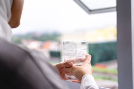 woman facing in the window holding a glass of cold water with ice cubes