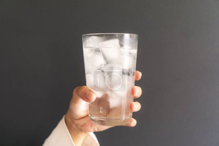 woman holding a glass of cold water with ice cubes, dark gray backround