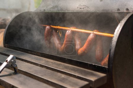 Sausages hanging on rack in a offset smoker with a thick smoke, closed up