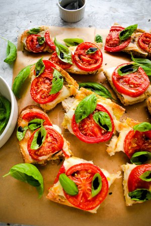 Tasty bruschetta with mozzarella, tomatoes and basil on a brown baking paper. Italian antipasti snacks set. Top view, grey background. Traditional Italian snack.