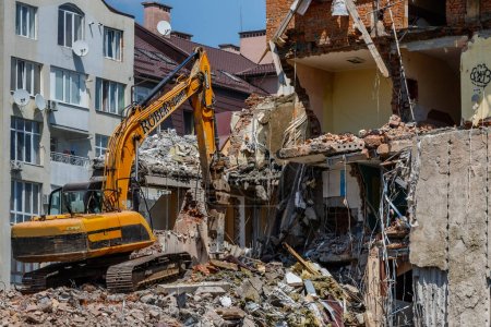 Téléchargez les photos : Uzhhorod, Ukraine - 23 mai 2023 : Excavatrice travaillant à la démolition d'un ancien bâtiment dans l'un des quartiers de la ville. - en image libre de droit