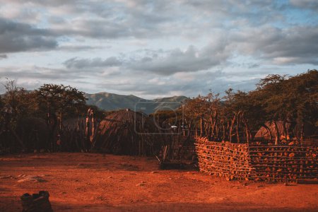 This captivating photograph captures the serene beauty of a South African village at sunset, with traditional huts and a dramatic sky, perfect for travel and cultural content.