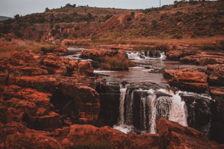 A serene view of Burks Luck Potholes and a nearby waterfall in South Africa, highlighting the tranquil flow of water over the rugged rock formations, perfect for captivating stock footage.