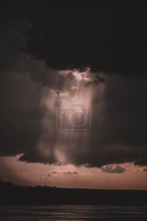 Eine fesselnde Aufnahme von Sonnenstrahlen, die durch dunkle Gewitterwolken über dem Sambesi durchdringen, schafft eine ätherische und dramatische Szene, die perfekt ist, um visuellen Projekten atmosphärische Tiefe zu verleihen.