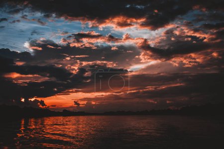 A stunning image capturing the vibrant colors of a sunset symphony over the Zambezi River with fiery reds, oranges, and purples illuminating the sky and reflecting on the water creating a dramatic scene.