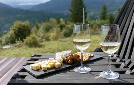 Photo for Two glasses of white wine and plate of cheese and grapes on table outdoor - Royalty Free Image