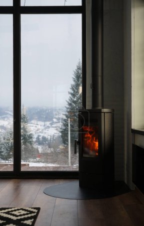 Téléchargez les photos : Cheminée moderne dans une maison confortable avec vue sur la montagne enneigée - en image libre de droit