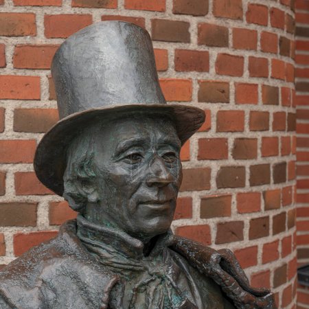 estatua de bronce sonriente del escritor H. C. Andersen contra una pared de ladrillo en Odense, Dinamarca, 19 de abril de 2024