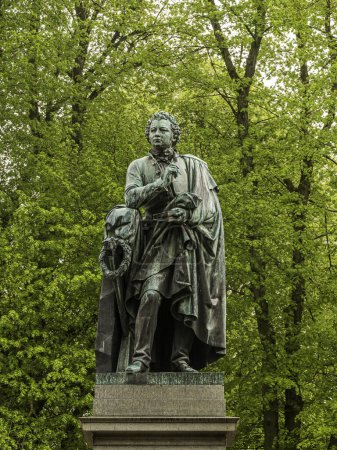 bronze staue of the writer Esaias Tegner against a green foliage at Lundagard, Lund, Sweden, May 6, 2024