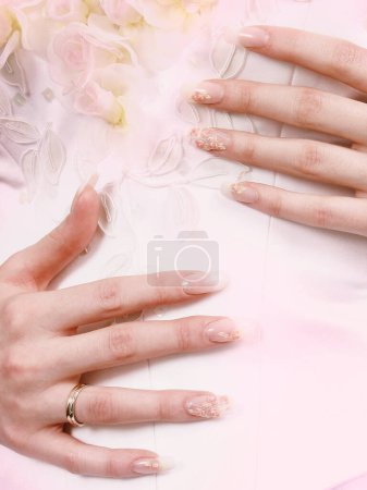 Weibliche Finger mit langen Nägeln auf dem Hintergrund eines Brautkleides.