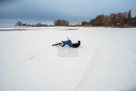 A boy fell off his bike while riding on a snowy river bank