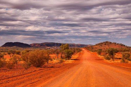 Outback road near Alice Springs in the Northern Territory, Australia, stretches through the vast, rugged landscape, offering a quintessential journey into the heart of the Australian Outback