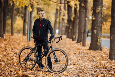 Foto de Joven hombre bastante atlético de pie con bicicleta en el parque de otoño. - Imagen libre de derechos