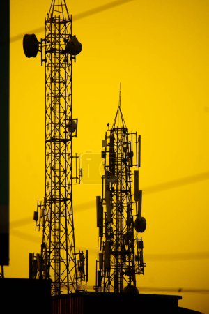 Two silhouette telephone towers stand tall against a vibrant yellow and orange sunset sky.