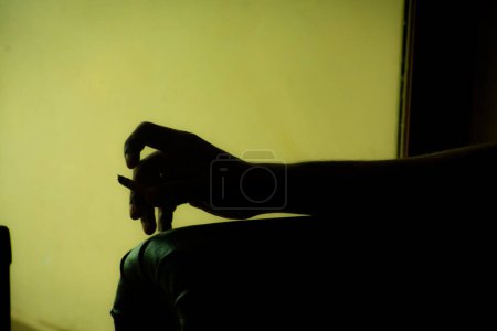 The silhouette of a hand holding a cigarette stands out against a bright backdrop, emphasizing a moment of reflection.