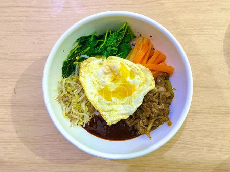 Vue du dessus du plat coréen nommé Bibimbap avec riz, légumes, ?uf et boeuf avec sauce coréenne servi dans un bol blanc
