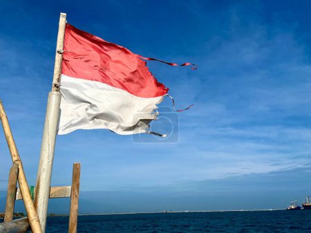 Drapeau indonésien agitant dans le vent fort attaché sur un bateau à mât de bambou en bois naviguant sur la mer