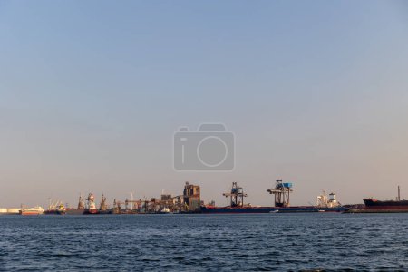 Ships float across the North Sea. Windmills in the background. Sea port in the Netherlands. A lot of cranes for loading goods. Different ships and barges.