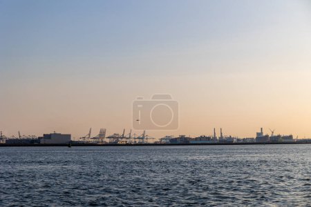 Schiffe fahren über die Nordsee. Im Hintergrund Windmühlen. Seehafen in den Niederlanden. Viele Kräne zum Verladen von Waren. Verschiedene Schiffe und Lastkähne.