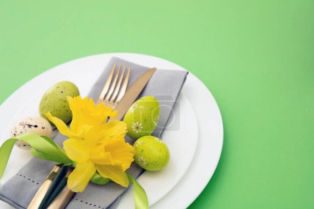 Photo for Easter table setting, Spring flowers and eggs decoration, napkin and golden cutlery on white plates, pastel green background - Royalty Free Image