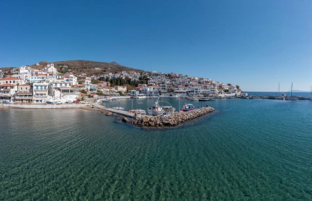 Photo for Andros island, Batsi village, Cyclades Greece. View of seafront whitewashed building, port, moored boat, clear transparent sea water blue sky. - Royalty Free Image